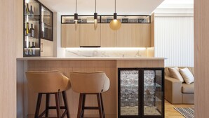 A modern kitchen with a marble countertop, wooden cabinets, and two bar stools. - Apartment Skopje Diamond  View (Skopje)