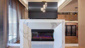 Una sala de estar moderna con chimenea empotrada, un televisor de pantalla plana montado encima y una zona de cocina al fondo.