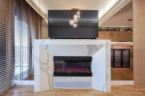 A modern living room with a built-in fireplace, a flat-screen TV mounted above it, and a kitchen area in the background.