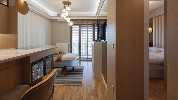Una habitación de hotel moderna con piso de madera, un sofá, una mesa de comedor y un televisor al fondo.