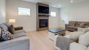 Ein modernes Wohnzimmer mit Kamin, zwei Sofas, einem Couchtisch und einem an der Wand befestigten Fernseher.