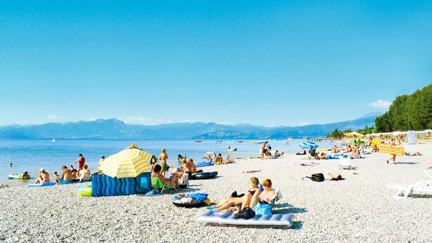Una playa con gente tomando el sol, nadando y usando flotadores inflables.