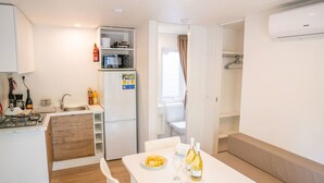 Cocina compacta con estufa, lavamanos y microondas. Hay una mesa de comedor con sillas y una botella de vino.