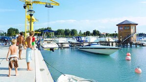 Un puerto deportivo con barcos amarrados, una torre de socorristas y una grúa amarilla.