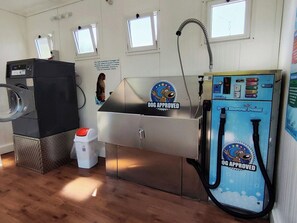 A room with a washing machine, a sink with a 'Dog Approved' sign, and a blue machine with a hose.