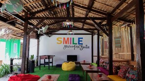 A cozy, rustic room with a thatched roof, a large wall mural saying "SMILE You're in Port Barton", and a comfortable seating area with a bean bag, tables, and a TV. - Garpeza Backpackers (San Vicente)