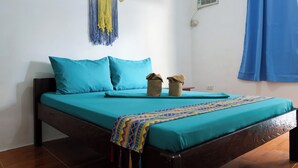 A bed with teal bedding, a colorful blanket, and two small baskets on the nightstand. - Garpeza Backpackers (San Vicente)