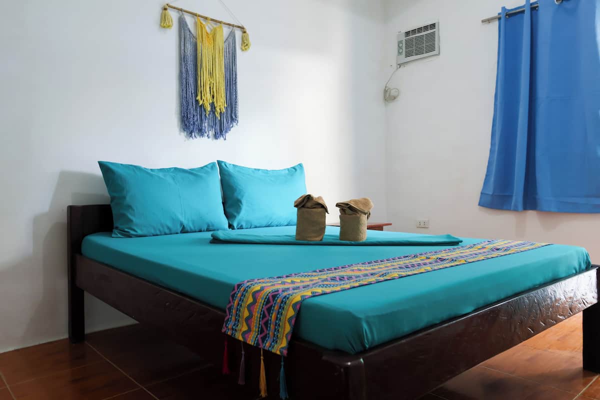 A bed with teal bedding, a colorful blanket, and two small baskets on the nightstand.
