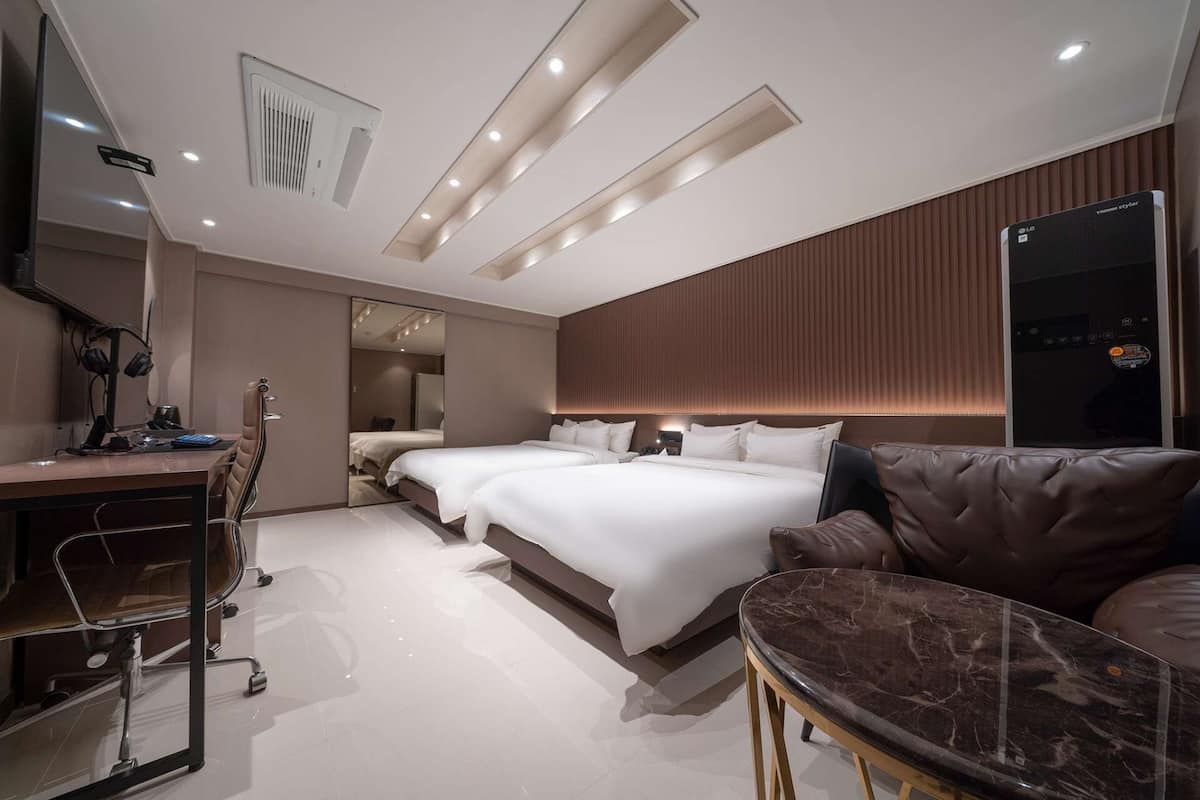 Une chambre d’hôtel moderne équipée d’un bureau, de deux lits, d’un canapé en cuir et d’un grand miroir.