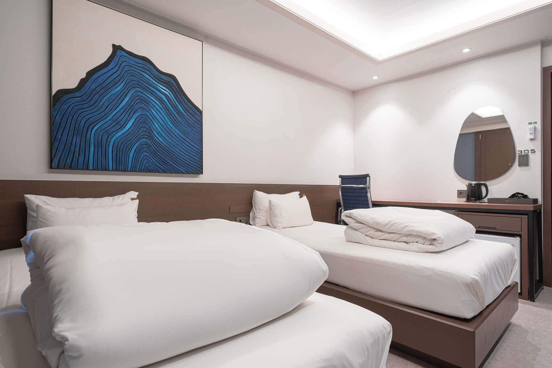A hotel room with two beds, a large abstract painting, a mirror, and a coffee machine.