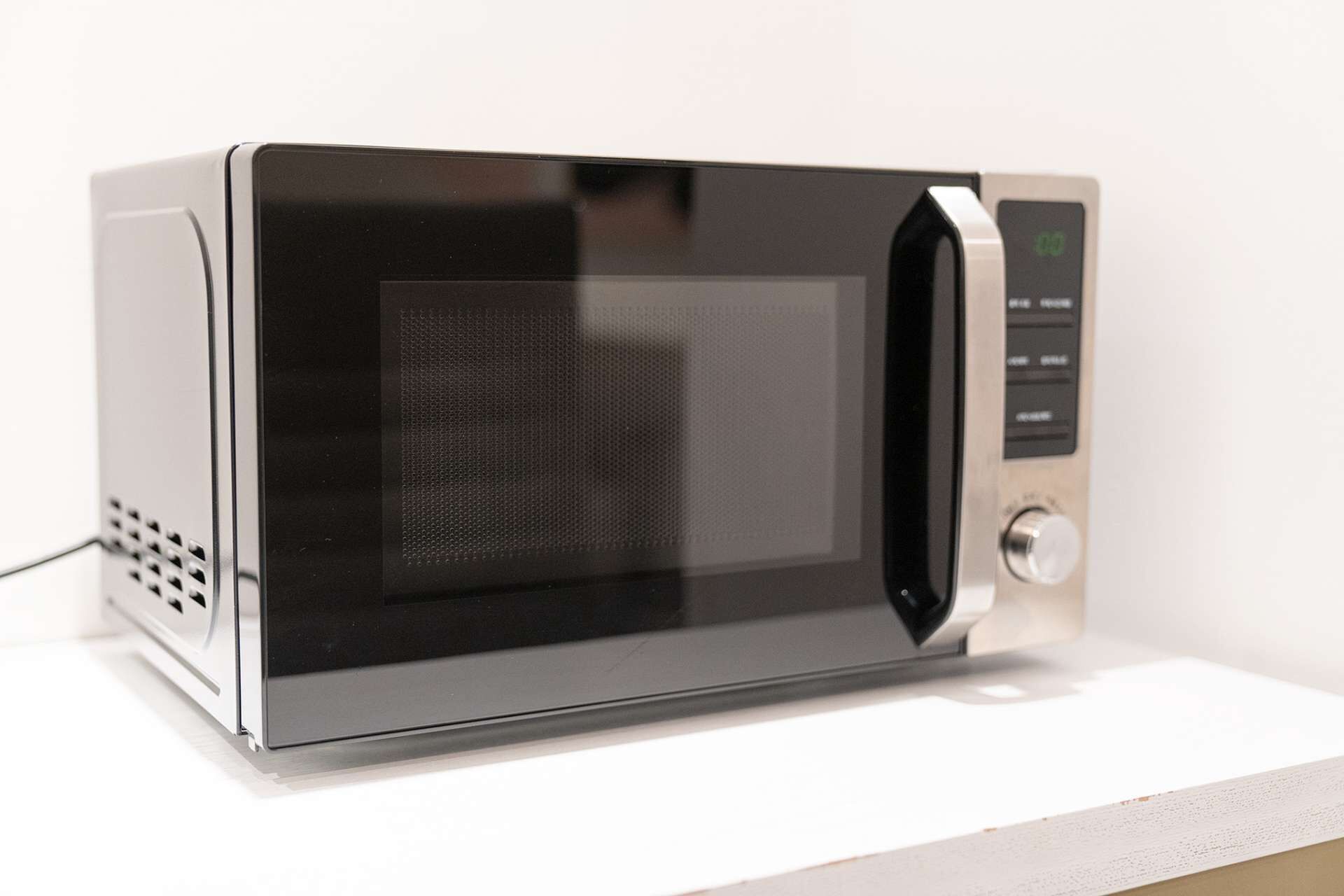 A microwave oven with a digital display, a control panel with buttons, and a power cord.