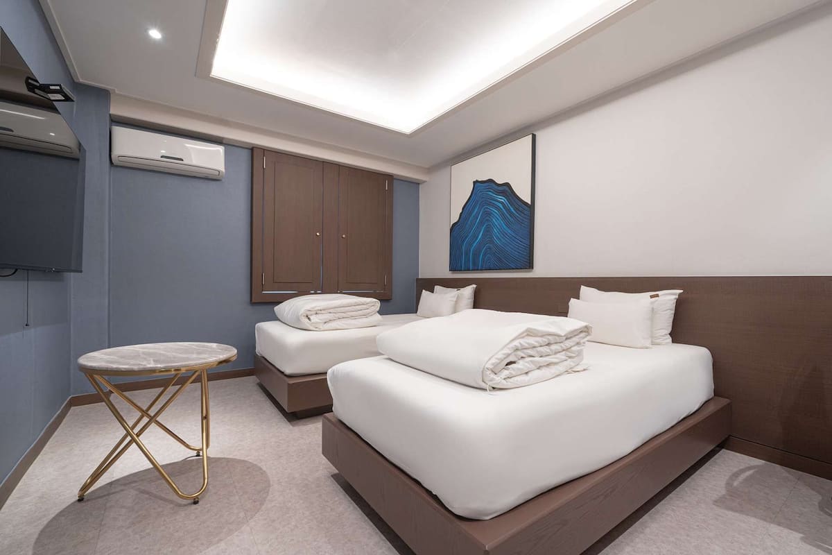 Une chambre d’hôtel moderne avec un grand lit, un plus petit lit, une table ronde et un luminaire au plafond.