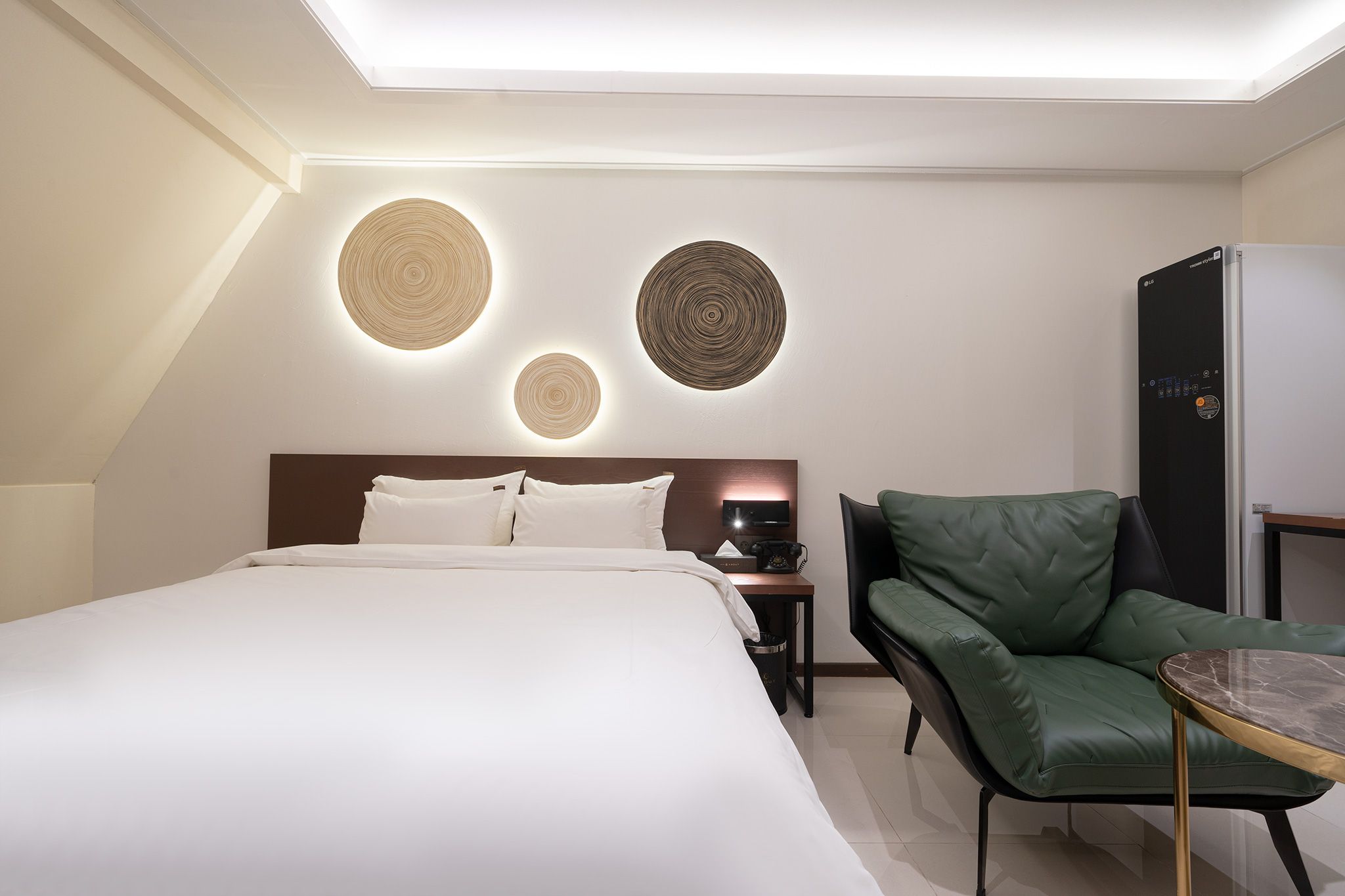A modern hotel room with a large bed, a green leather chair, a small table, and a minibar.