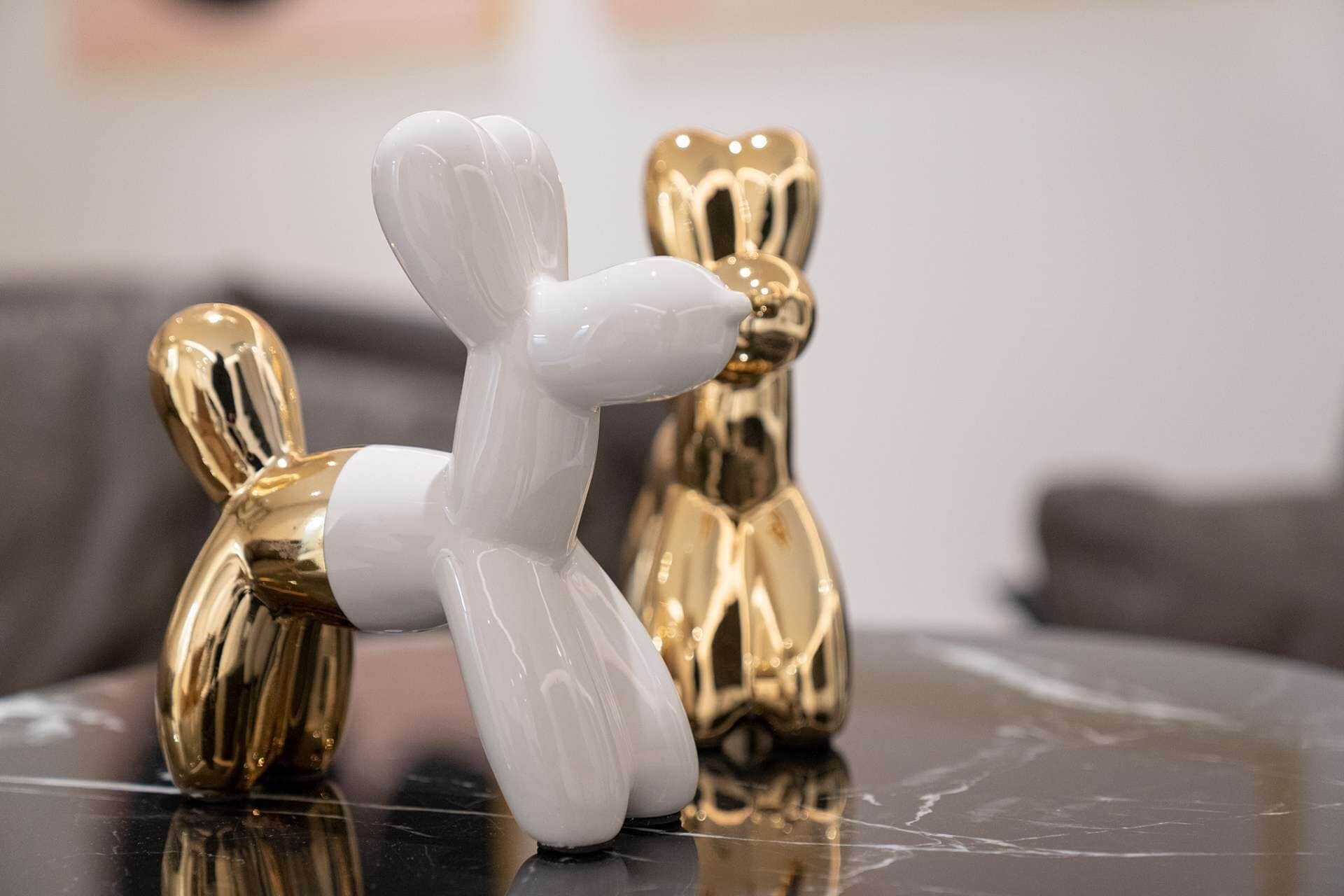 Deux objets décoratifs, l’un blanc et l’autre doré, posés sur une surface réfléchissante.
