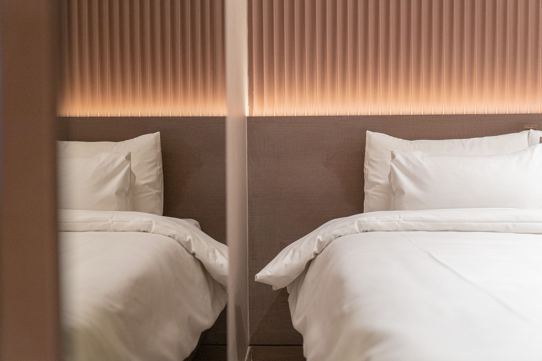 A hotel room with two beds, a headboard with vertical slats, and a mirror reflecting the room.