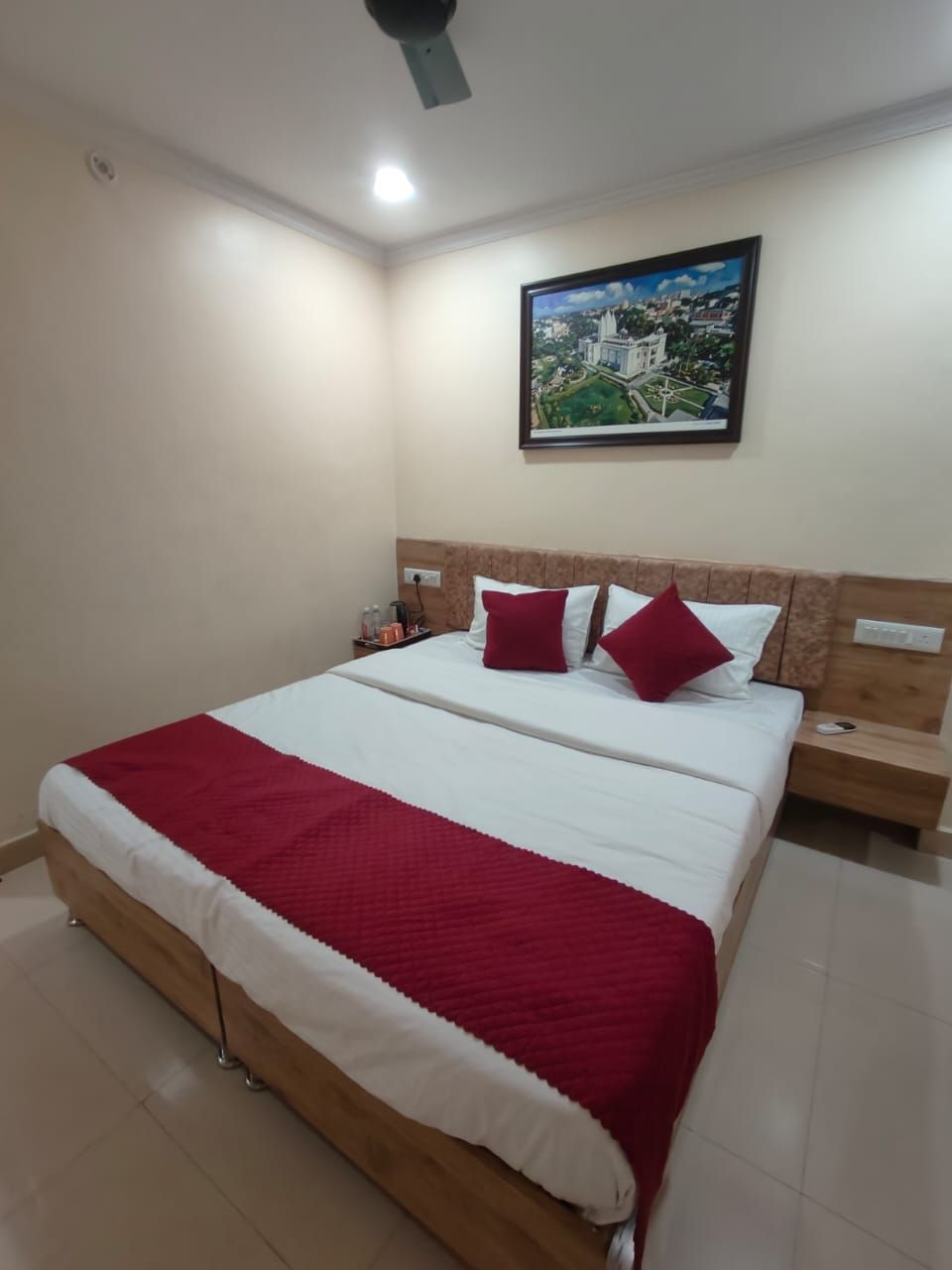 A neatly made bed with a red and white bedspread, a wooden headboard, and a nightstand with a lamp.