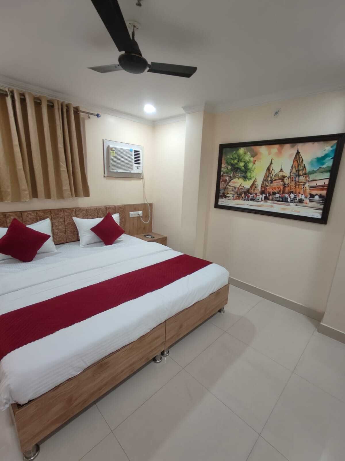 A bedroom with a bed, a ceiling fan, an air conditioning unit, a nightstand, a framed picture on the wall, and a tiled floor.