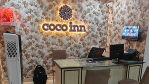 A Coco Inn reception desk with a floral wallpaper, a ceiling fan, and a television mounted on the wall. - Coco Inn Homestay  (Varanasi)