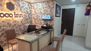 A reception area with a 'coco inn' sign, a TV mounted on the wall, a reception desk, and two chairs. - Coco Inn Homestay  (Varanasi)