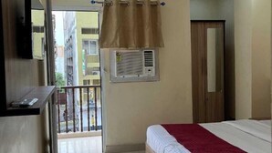 A hotel room with a bed, an air conditioning unit, a ceiling fan, a TV mounted on the wall, and a balcony with a view of the outside. - Coco Inn Homestay  (Varanasi)