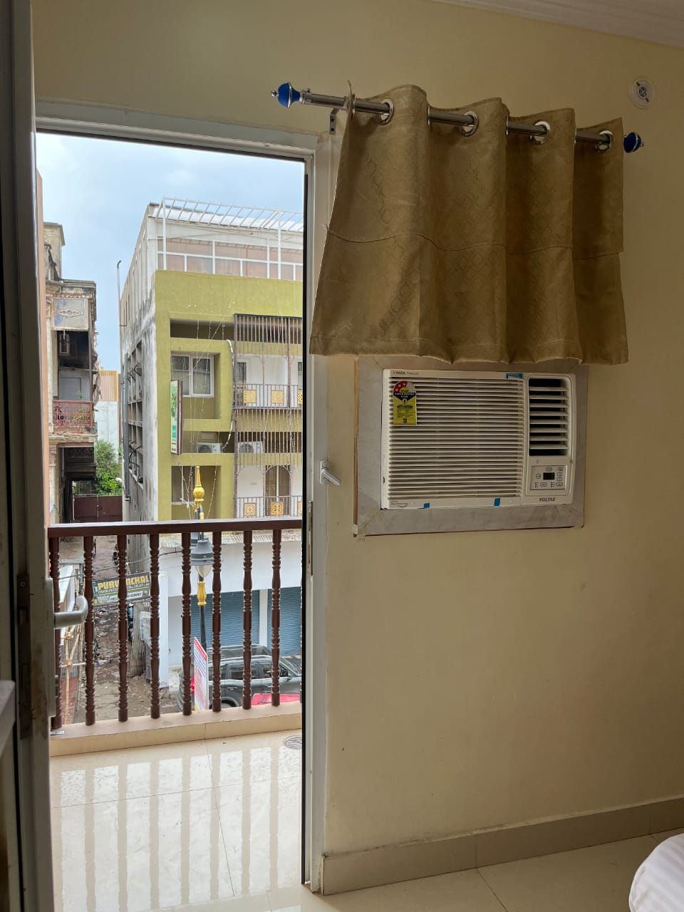 A room with a sliding glass door leading to a balcony, a wall-mounted air conditioner, and a view of neighboring buildings.