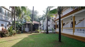 A courtyard with a grassy area, palm trees, and buildings with balconies and a staircase. - Joy Guest House (Calangute)