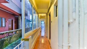 A corridor with a tiled floor, a railing on one side, and a building with a red facade on the other. - Joy Guest House (Calangute)