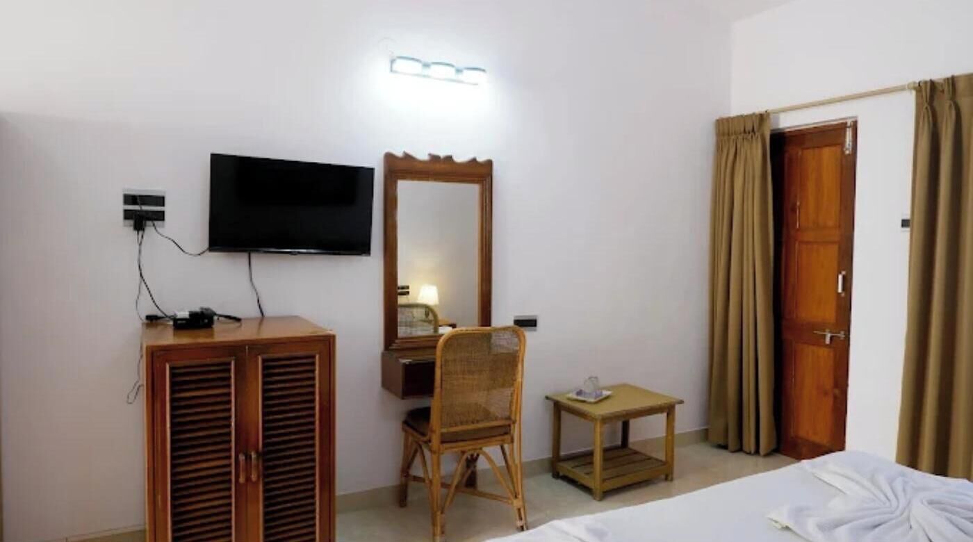 A hotel room with a bed, a desk with a chair, a television, and a wardrobe.