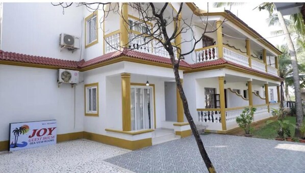 A two-story building with a white facade and yellow trim, featuring a balcony and a sign for "JOY Guest House Sea View Rooms". - Joy Guest House (Calangute)