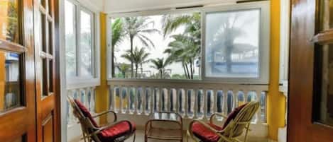 A room with two wicker chairs, a small table, and a view of palm trees through large windows.