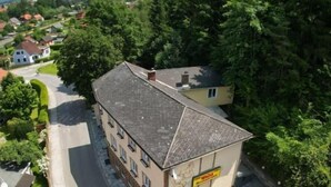 A building with a sloped roof, a sign indicating a restaurant, and a parking area with several cars. - Waldrestaurant Vida  (Kapfenberg)