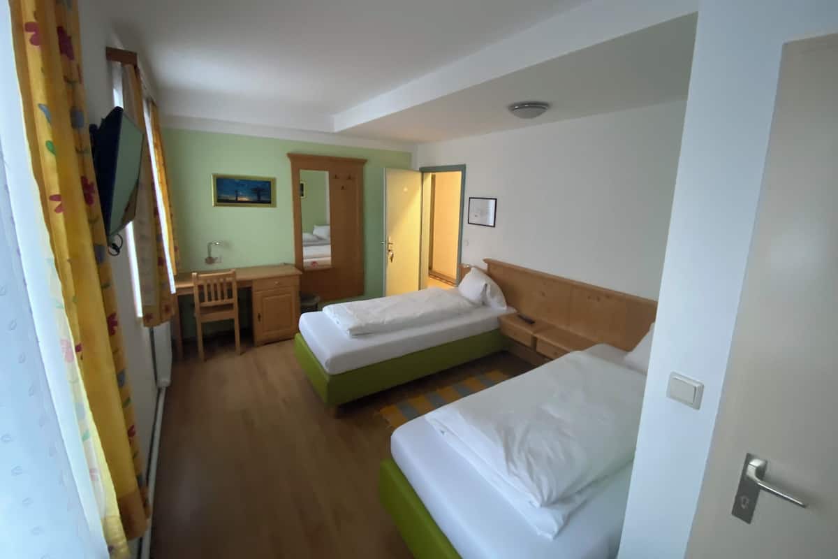 A hotel room with two beds, a desk, a chair, and a wardrobe.