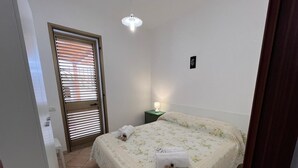 Et soveværelse med seng, natbord, lampe og dør med skodder.