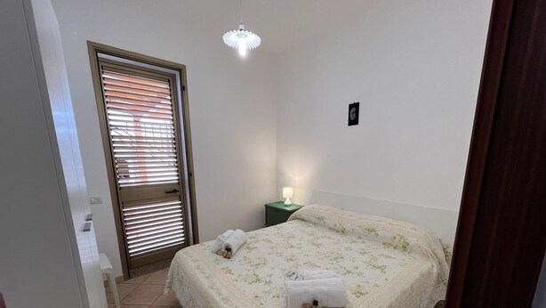 Une chambre à coucher avec un lit, une table de chevet, une lampe et une porte avec des stores.