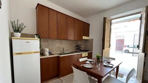 Et kompakt køkken med træskabe, et hvidt køleskab og et spiseområde med et bord og stole.