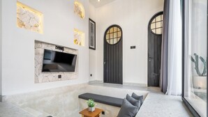 A modern living room with a stone fireplace, a flat-screen TV, a sofa, and a small table with a plant. - Casa Santisya 4 (Munggu)