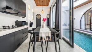 A modern kitchen with dark cabinets, a wooden ceiling, and a dining area with a table and chairs. - Casa Santisya 4 (Munggu)