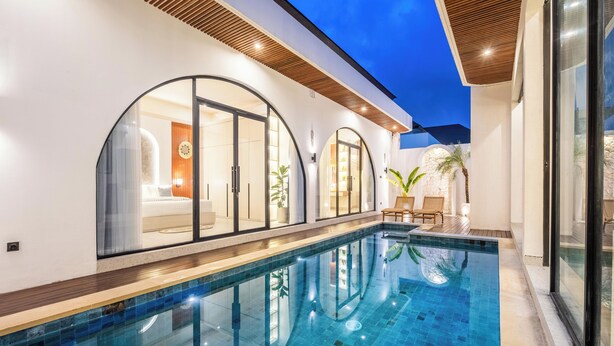 A modern indoor swimming pool with clear glass walls, a wooden deck, and a well-lit interior. - Casa Santisya 4 (Munggu)