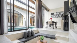 A modern living area with a curved sofa, a small wooden table with a plant, and a dining area with a table and chairs. - Casa Santisya 4 (Munggu)