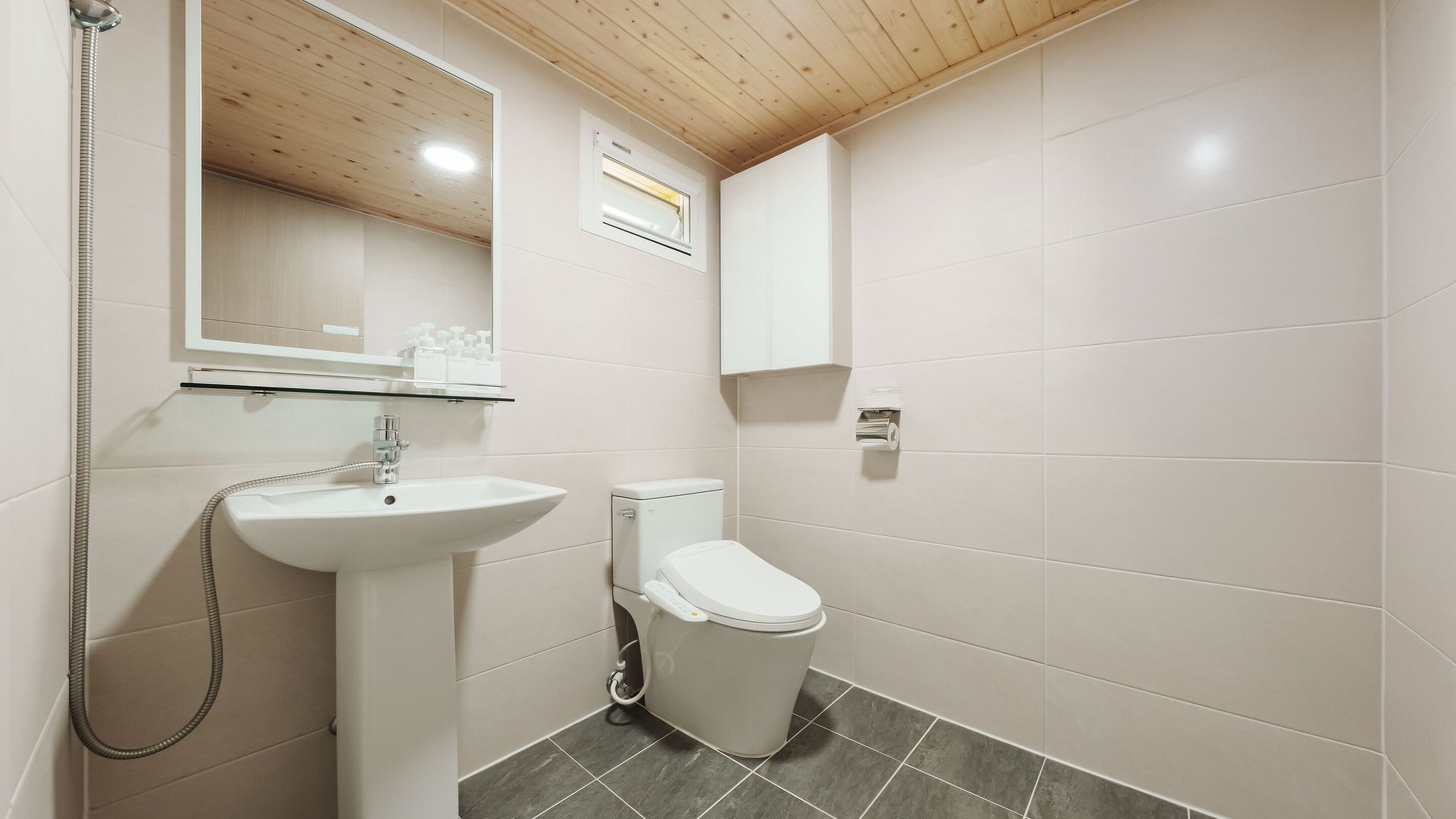 A bathroom with a white sink, toilet, and shower. There is a mirror above the sink and a window above the toilet.