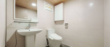 A bathroom with a white sink, toilet, and shower. There is a mirror above the sink and a window above the toilet.
