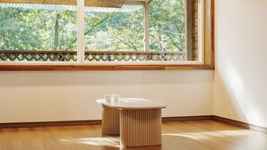 Una habitació amb terra de fusta, una taula blanca amb dues tasses blanques, i una finestra amb vista a arbres.