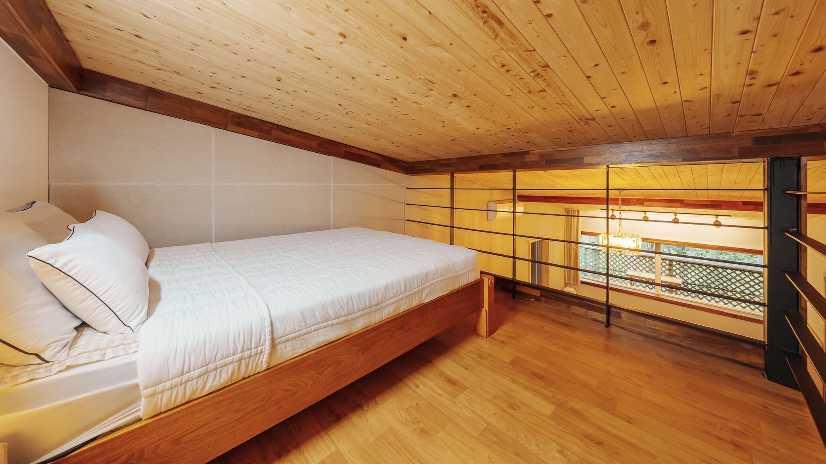 Un dormitorio con cama de madera, vista por una ventana con celosía y techo de madera.
