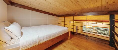 Un dormitorio con cama de madera, vista por una ventana con celosía y techo de madera.