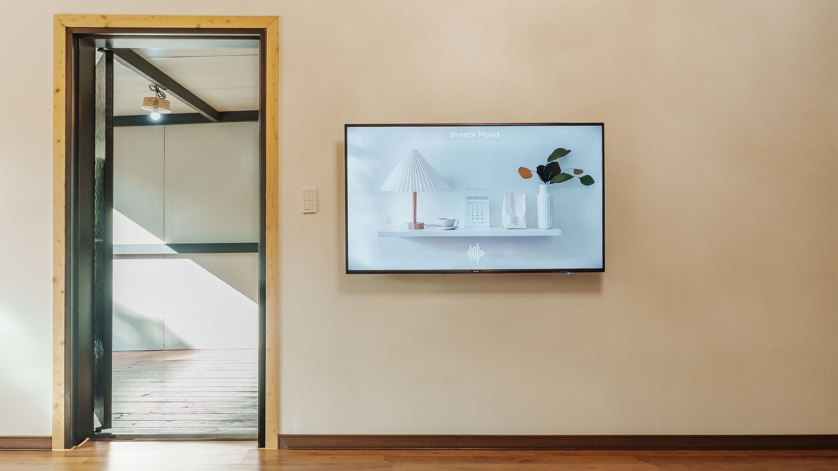 A room with a wooden floor, a glass door leading to a staircase, and a wall-mounted television displaying a serene indoor scene.