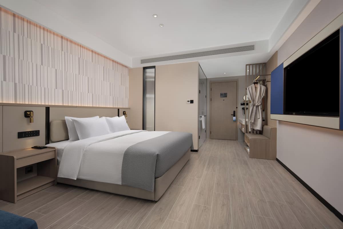 Quarto de hotel moderno com uma cama grande, televisão, guarda-roupa e casa de banho com chuveiro e sanita.