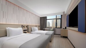 A hotel room with two beds, a desk, a chair, a TV, and a window with a city view. - Wanda Yuehua Hotel Tangshan North (Tangshan)