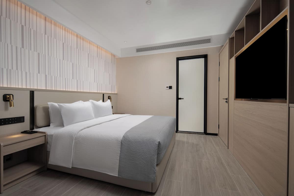 Quarto de hotel moderno com uma cama grande, uma mesa de cabeceira, um guarda-roupa e uma porta.