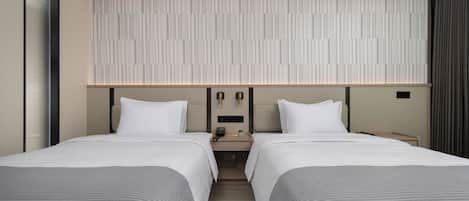 Une chambre d’hôtel moderne avec deux lits, une grande fenêtre, un panneau de commande fixé au mur et une table de chevet avec une lampe.