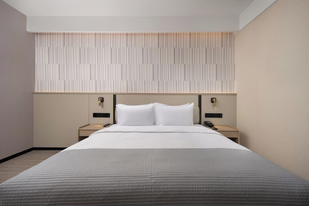 Une chambre d’hôtel moderne avec un grand lit, deux tables de chevet, un panneau lumineux fixé au mur et un téléphone sur chaque table.